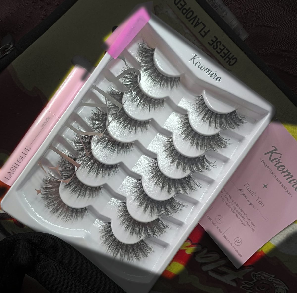 A lash pack: tray of seven wispy lash pairs with a pink lash glue tube and a pink thank-you care card